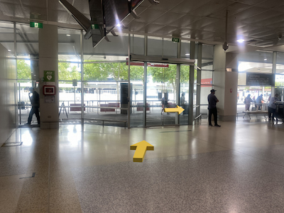 Glass doors at airport exit, people standing to the left and right of doors.